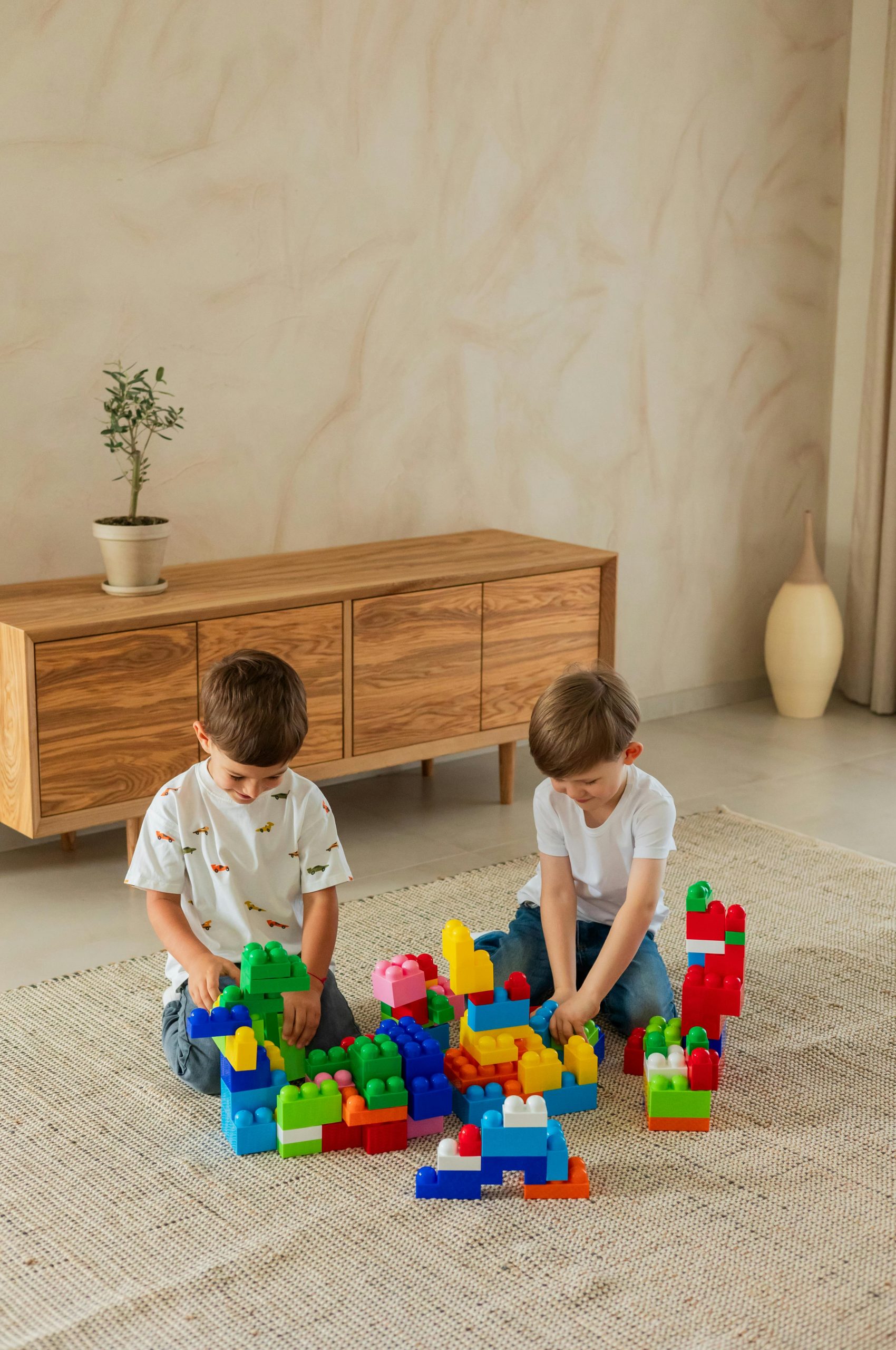 Two young boys playing with colorful building blocks on a rug indoors, fostering creativity and fun.
